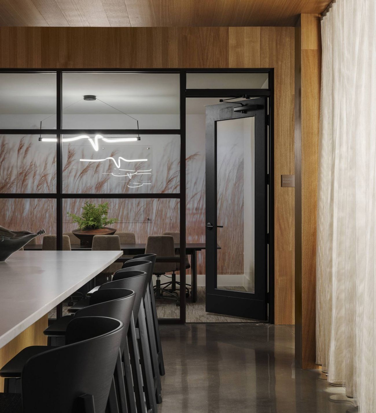 Leawood Village Modern office amenity with wooden walls, black chairs, and glass partition showing blurred outdoor scene.