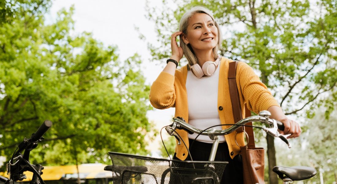 Middle aged woman walking a bike near a park
