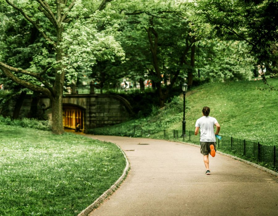 Man running through a beautiful city park with grass and trees