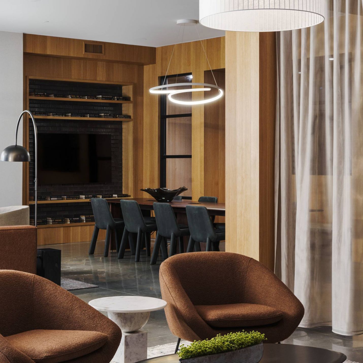 Leawood Village 
Modern club room with brown chairs, black coffee table, hanging lights, and a dining area in the background.