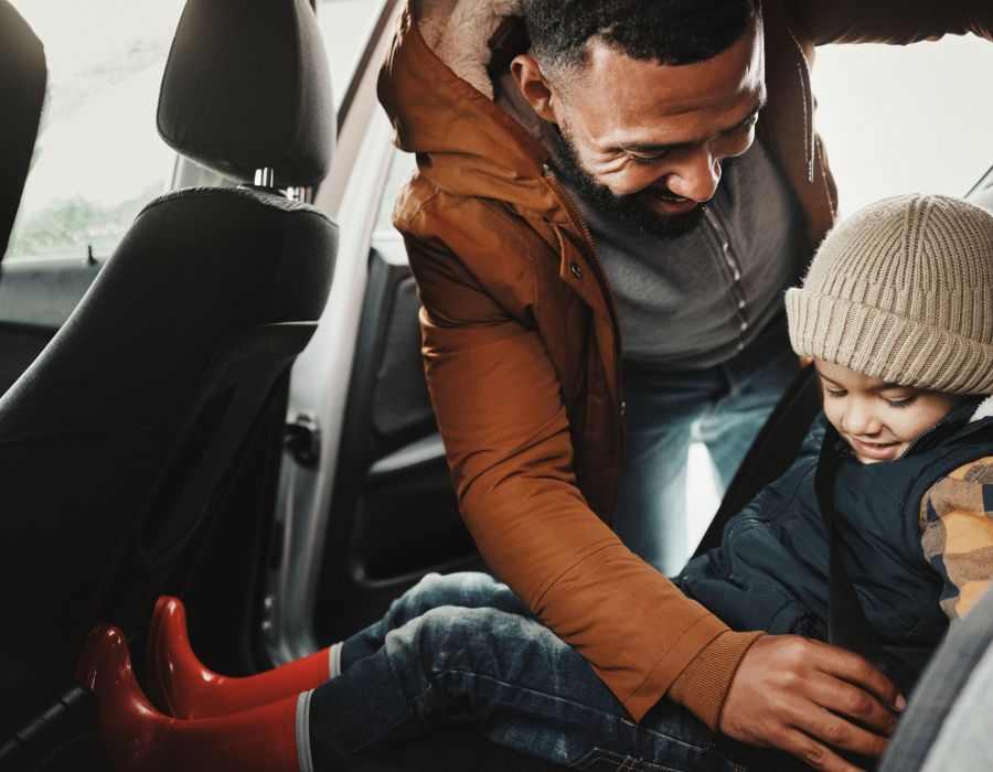 Father helping young son into his car seat